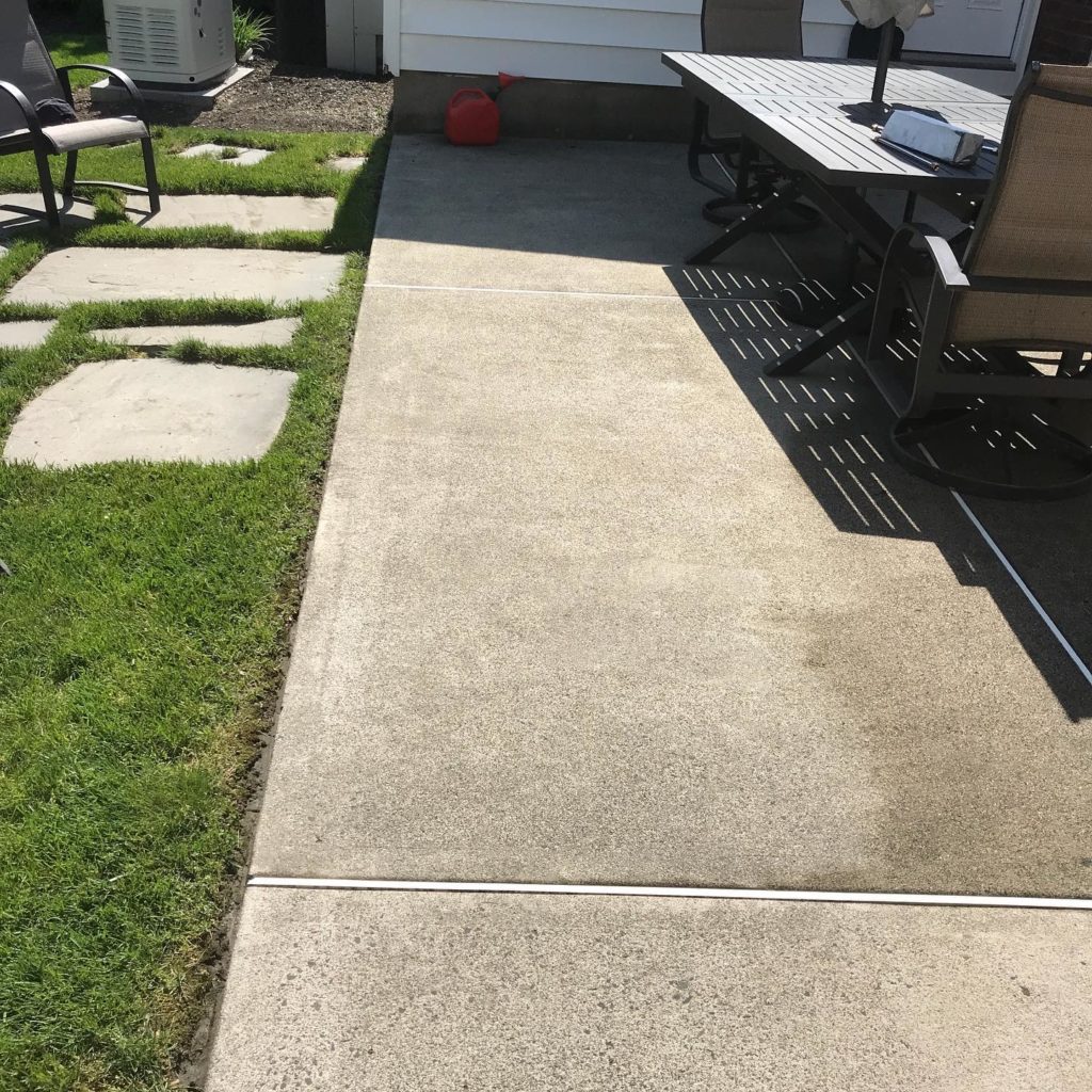 A concrete floor with a bench and chair nearby, set in a grassy area, creating a simple and serene outdoor seating arrangement