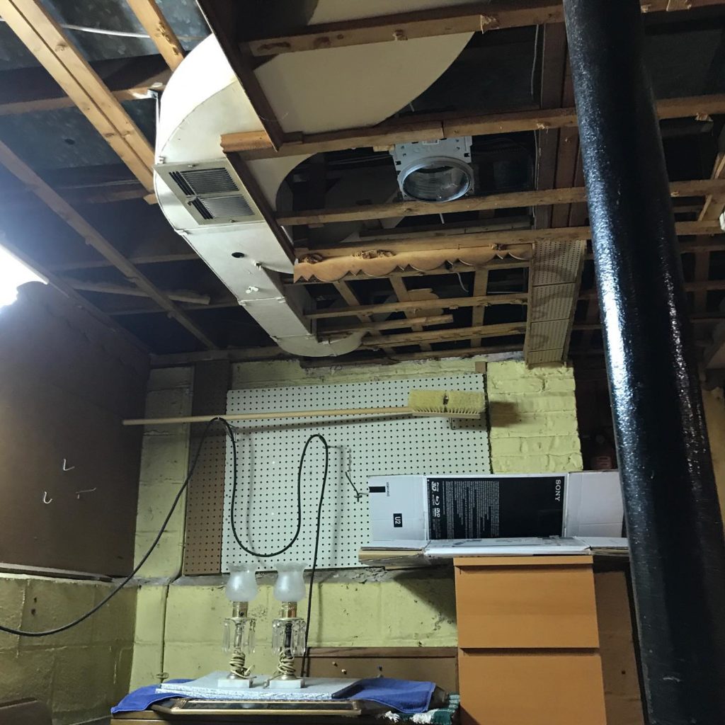 An untidy underground area with a damaged ceiling, showing debris scattered on the floor and visible cracks and holes in the ceiling tiles