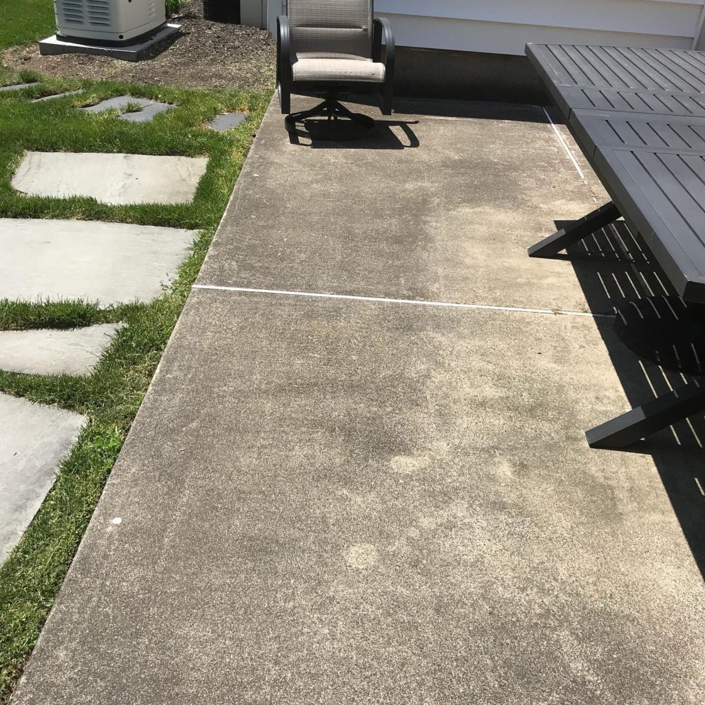 A concrete floor with a bench and chair nearby, set in a grassy area, creating a simple and serene outdoor seating arrangement