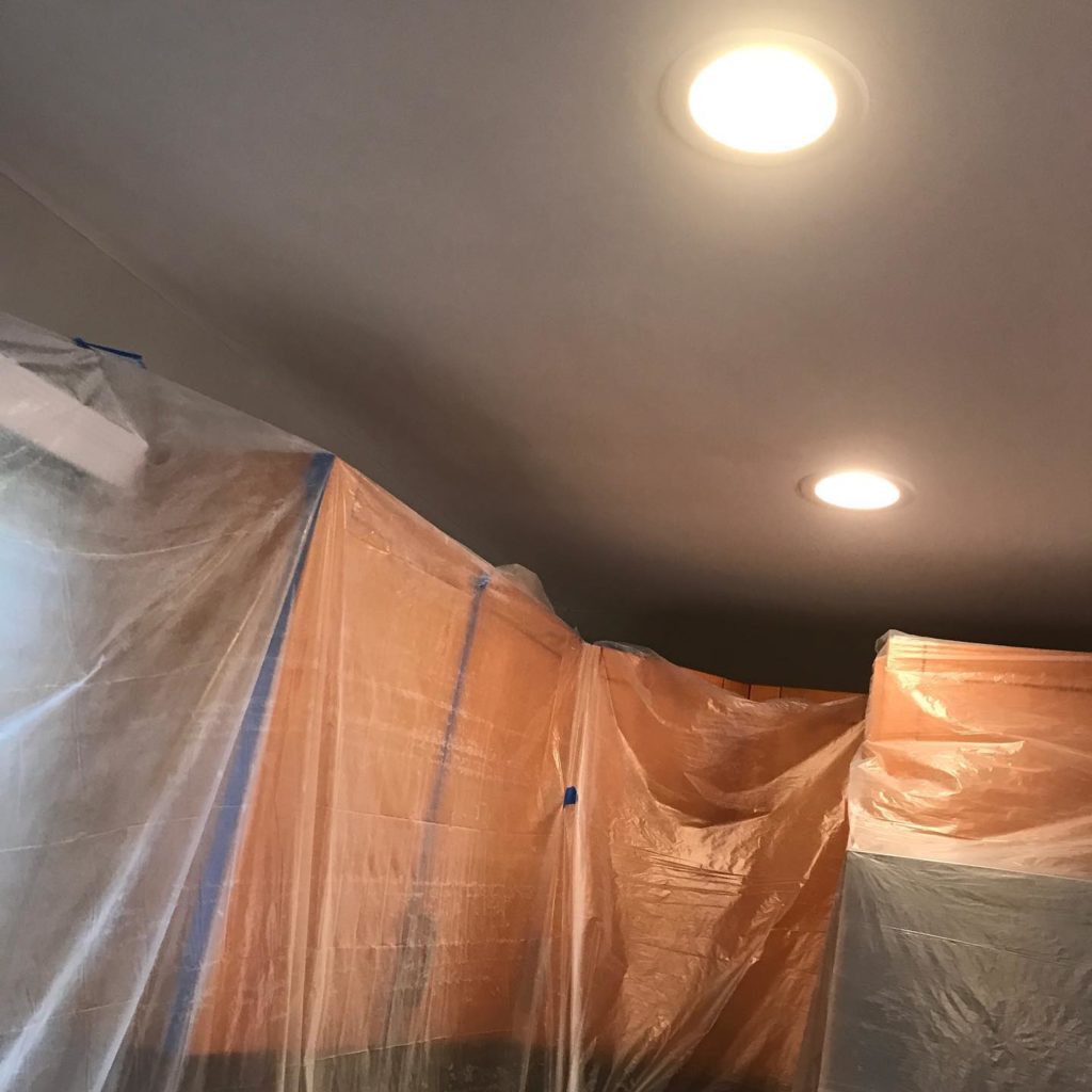 A room with items covered with glass sheets under lights, ready for painting work